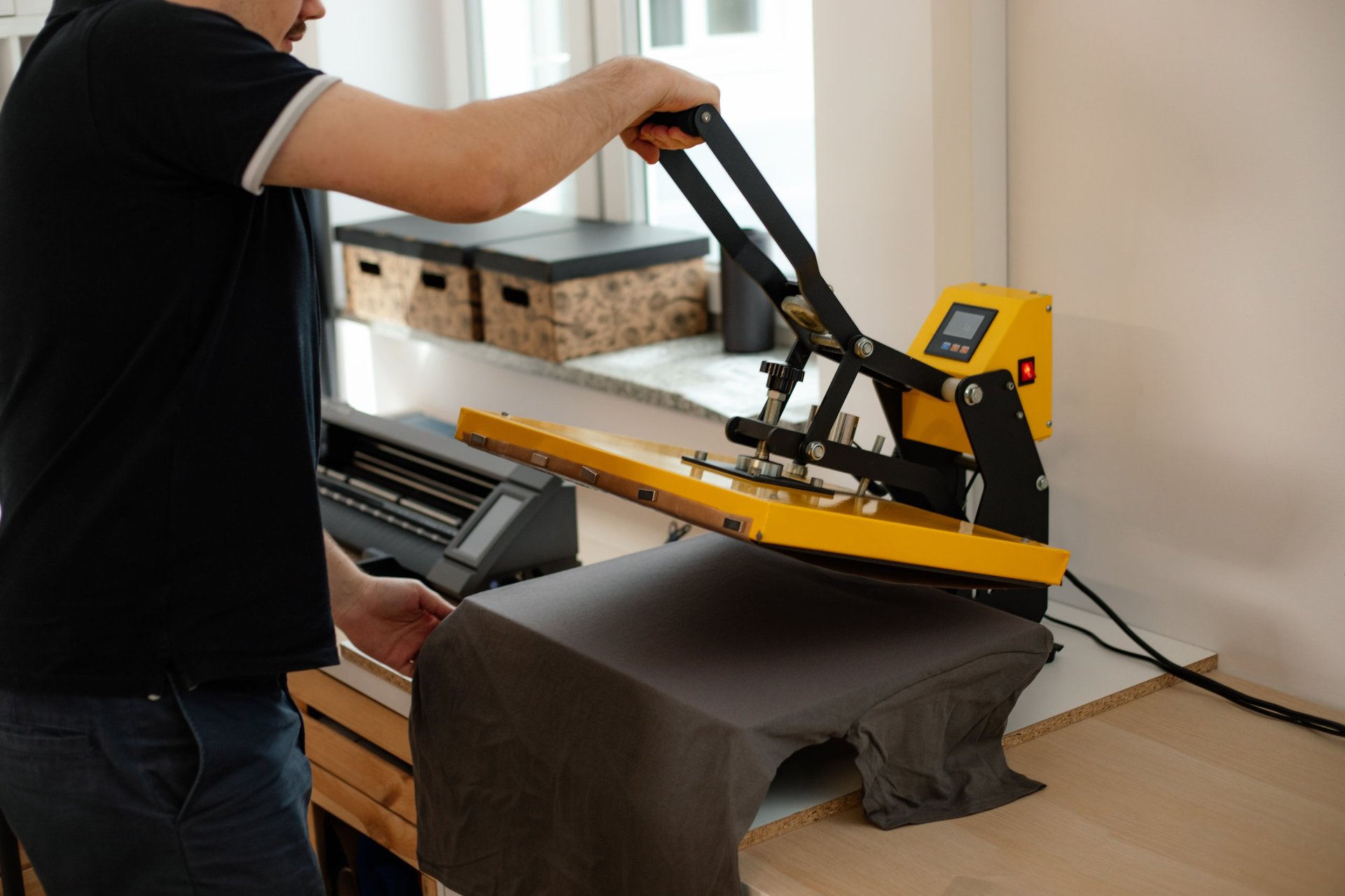 Cropped man worker side back using heat thermal textile application transfer press. Printing application black T-shirt design. Printing house office offset equipment. Manufacturing business fabric