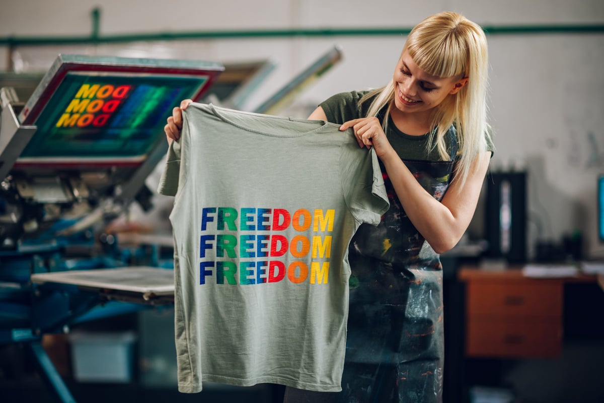 Smiling female printing workshop worker showing t-shirt