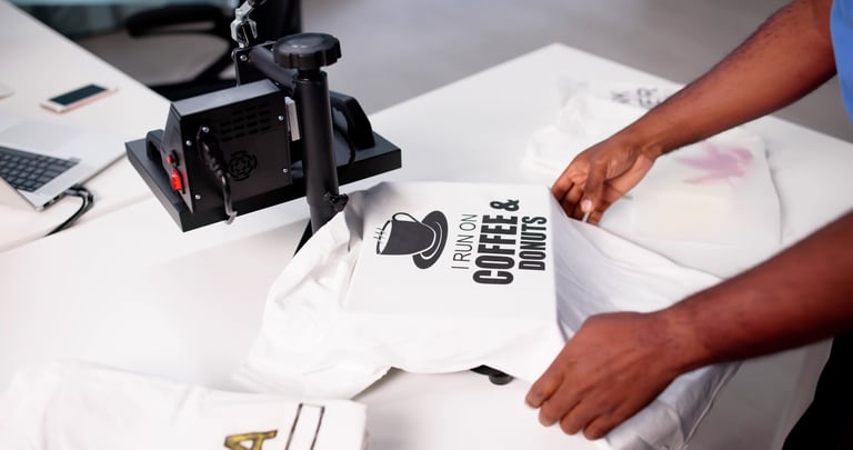 African-American man screen printing a custom logo t-shirt at a heat press factory