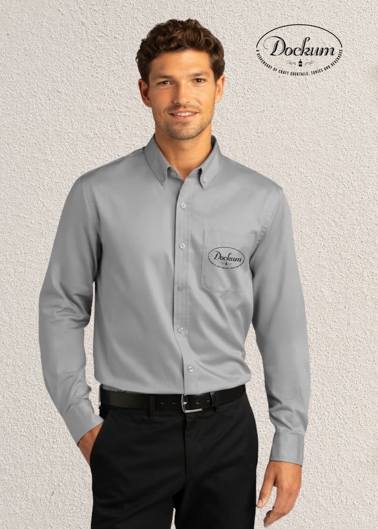 Man wearing gray button-up Dockum shirt with logo and black trousers against light background