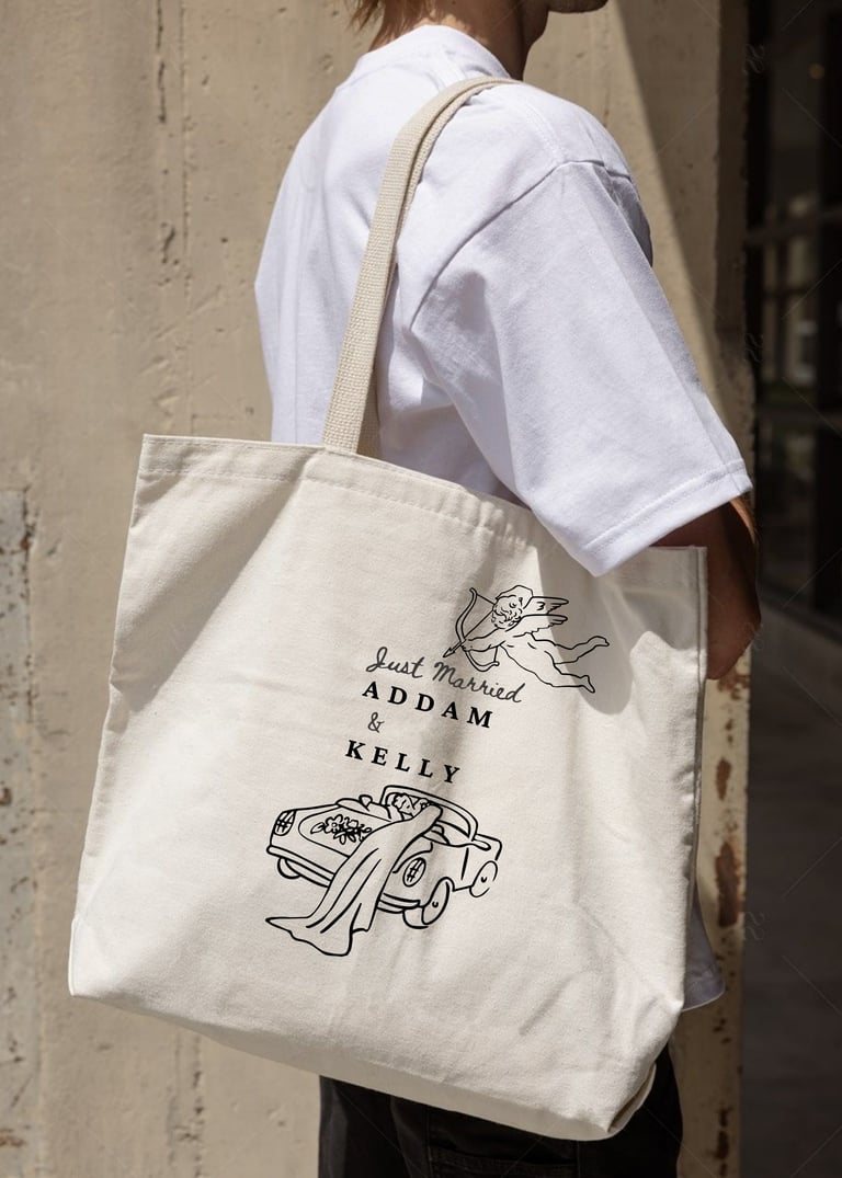 Person wearing white t-shirt carrying cream canvas tote bag with Cupid and car illustrations and text reading Just married ADDAM & KELLY