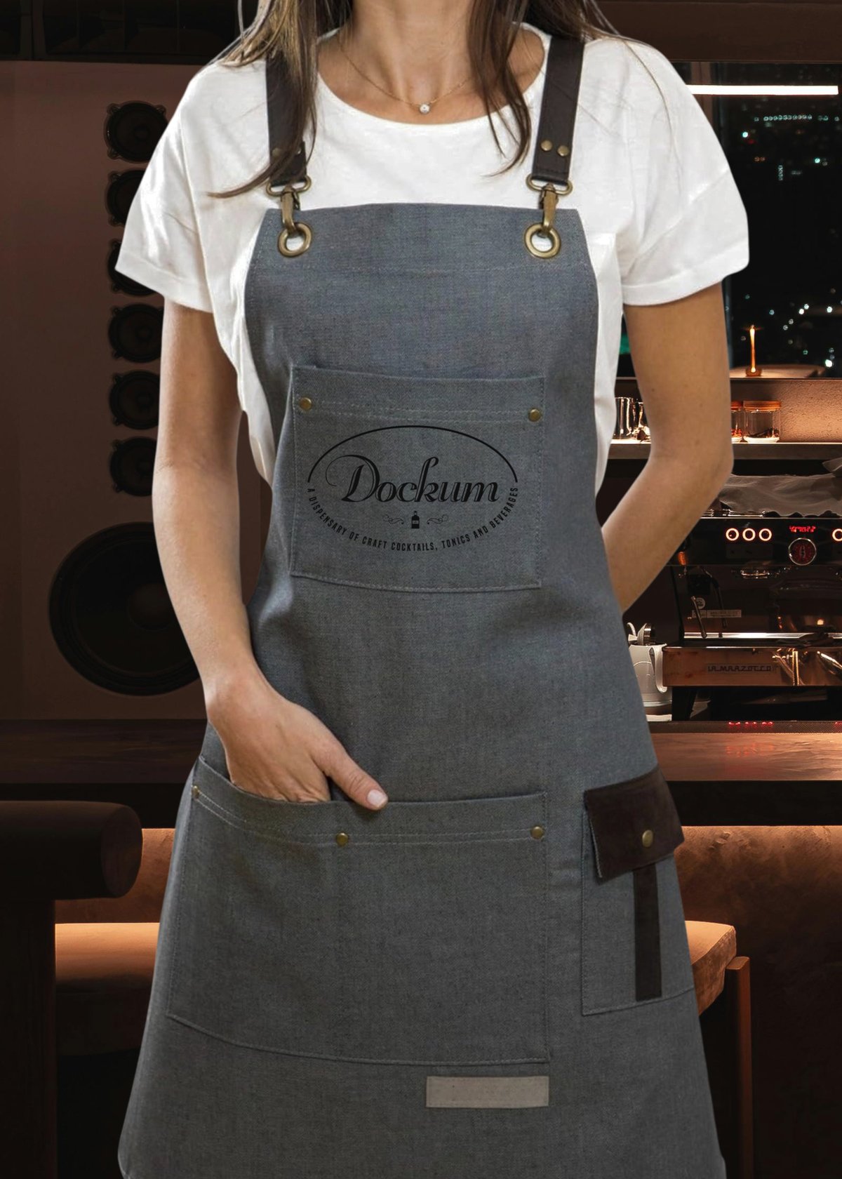 Woman wearing blue-gray Dockum apron with black straps over white t-shirt in modern kitchen setting