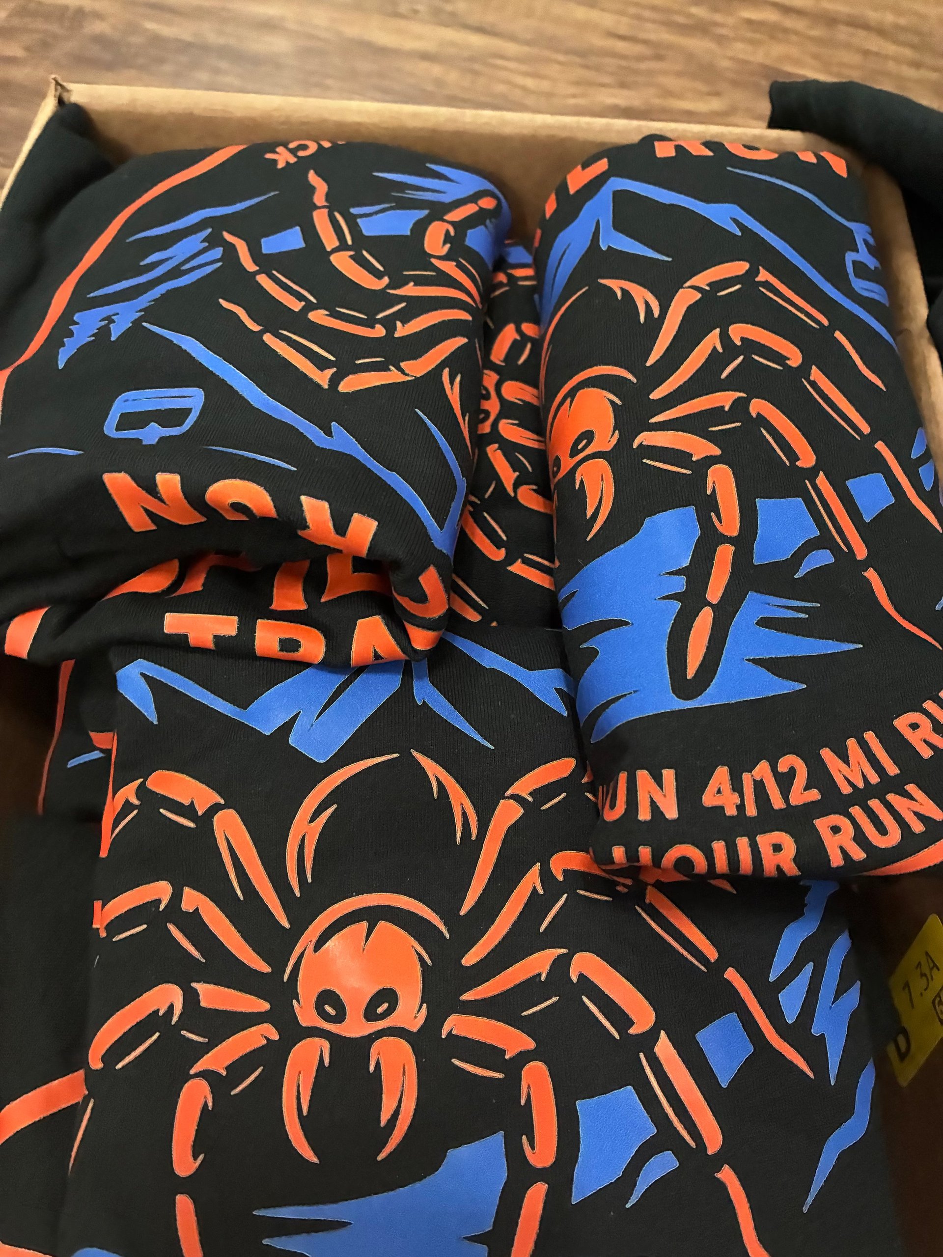 Black athletic socks with bold orange and blue spider designs and text, folded in packaging box