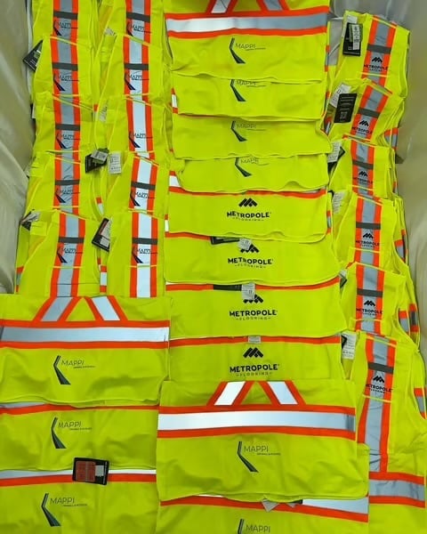 Collection of neon yellow safety vests with reflective stripes and Metropole branding displayed on white wall