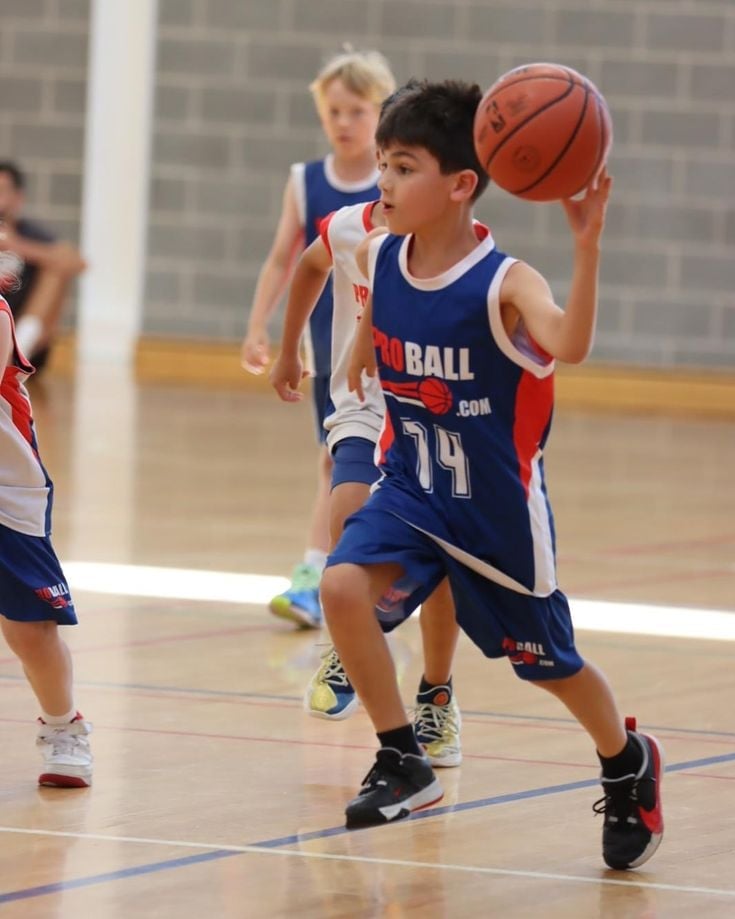 Young basketball player wearing number 14 jersey dribbling ball during youth game in indoor gymnasium