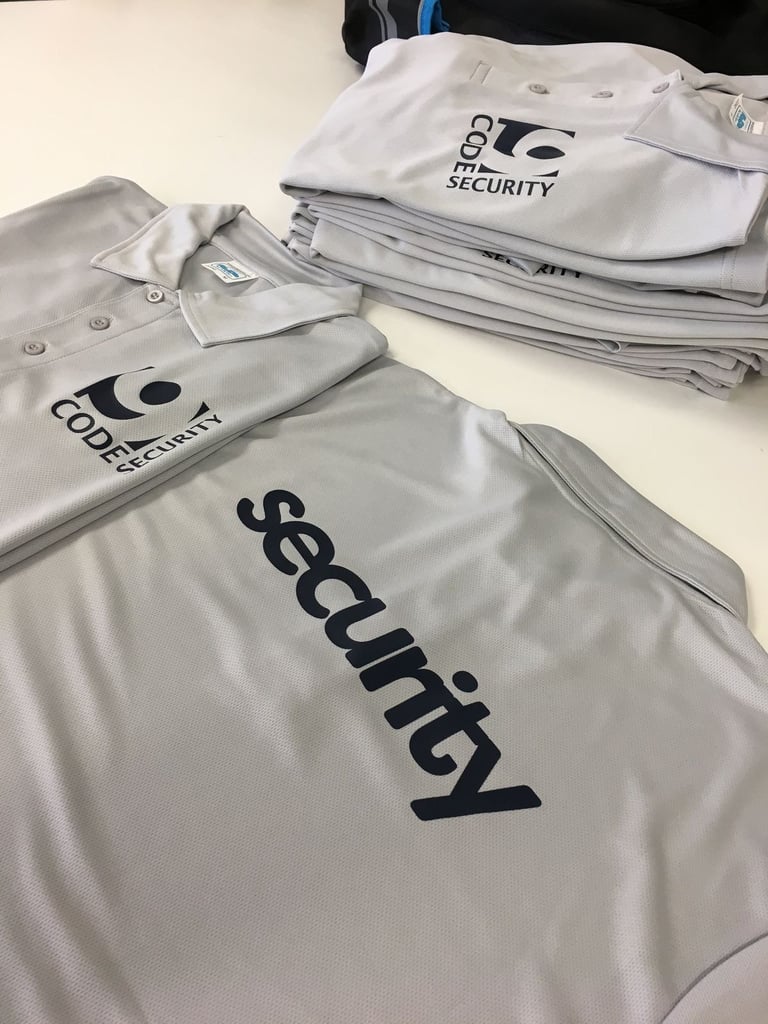 Folded code compliance and security branded polo shirts and jackets in white and gray on a table