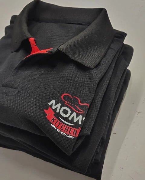 Black collared polo shirt with red embroidered MOM Kitchen logo and chef hat design