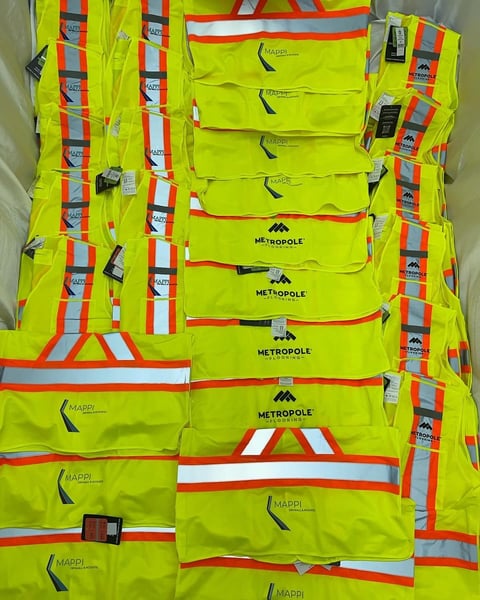 Collection of neon yellow safety vests with reflective strips and Metropole branding arranged and displayed