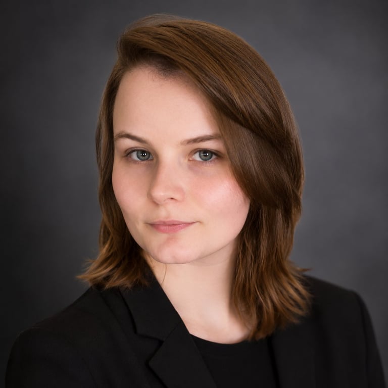 Professional headshot of a woman with shoulder-length brown hair wearing a black blazer against a gray background