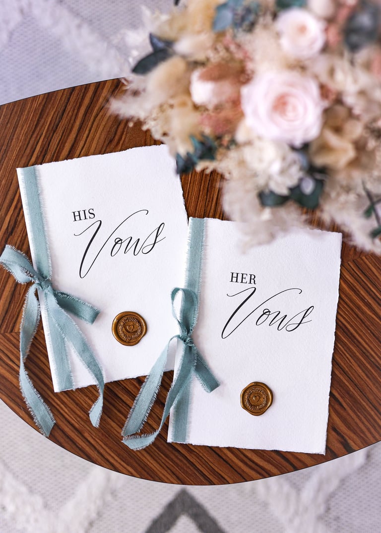 His and Her vow cards tied with blue ribbons and wax seals on wooden plate with flowers