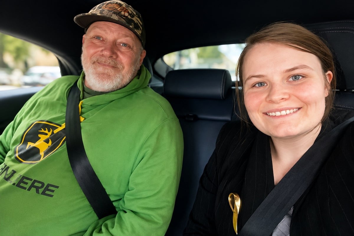 Adult man wearing green John Deere hoodie and cap sits next to smiling young woman in black jacket inside a car