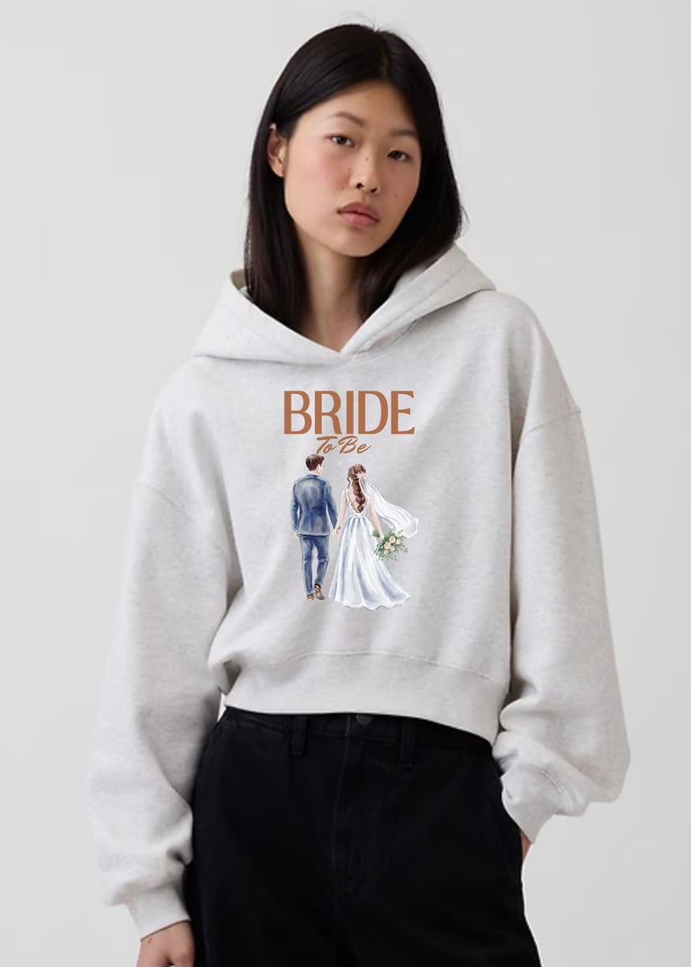 Woman wearing a light gray BRIDE hoodie with illustrated wedding couple graphic and black pants